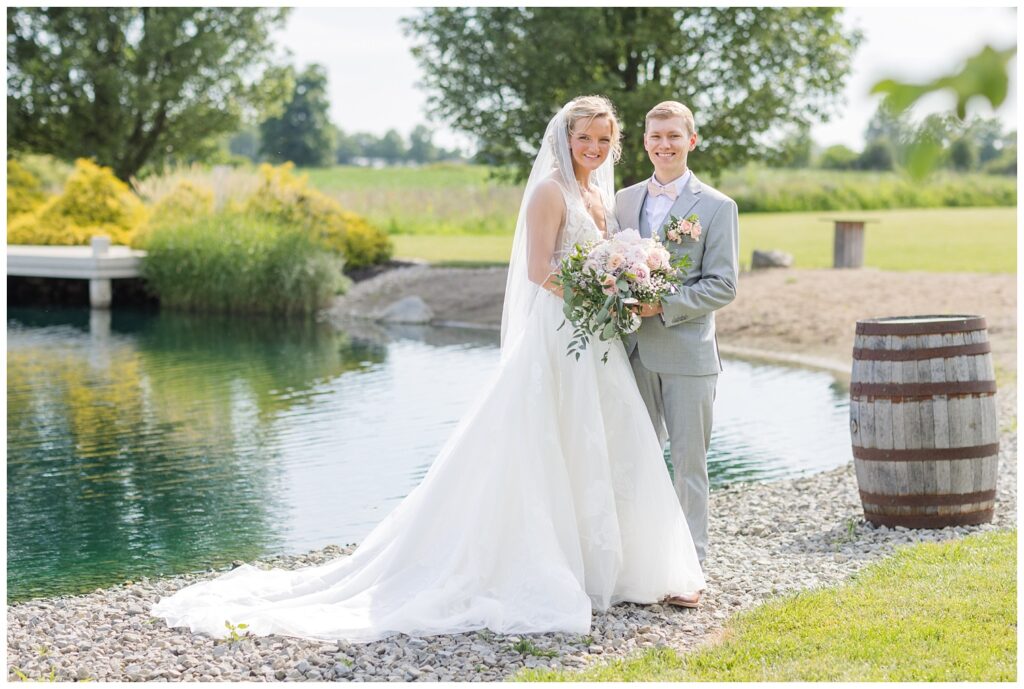 groom and bride posing next a barrel in front of the pond at Prairie Stone Farm