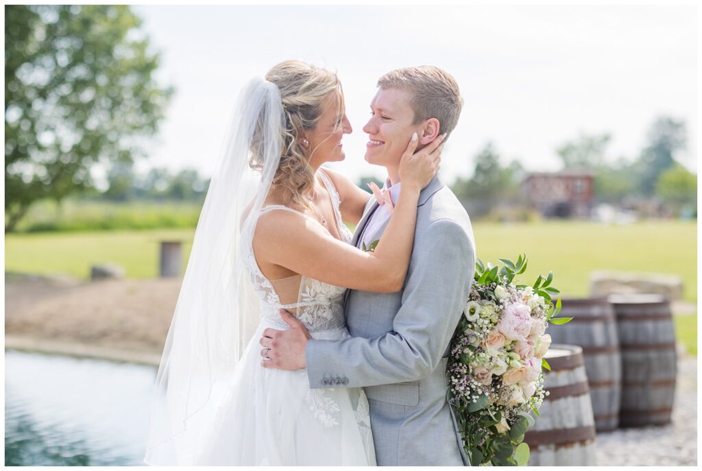 bride holding the groom's face and smiling near the pond at northwest Ohio wedding venue