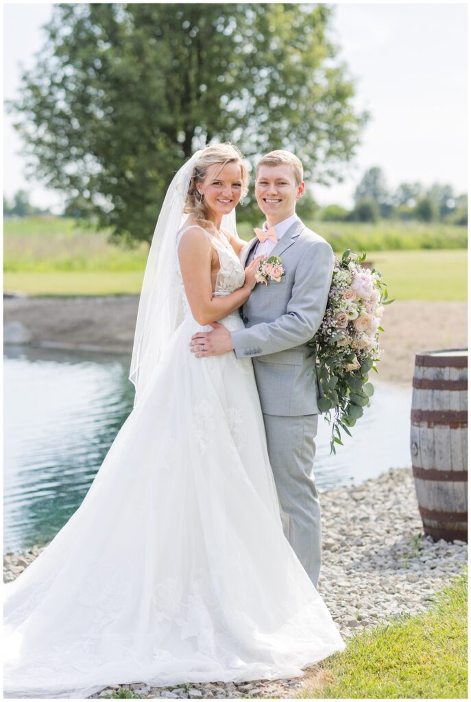 bride holding her bouquet behind the groom's back and smiling together in front of pond