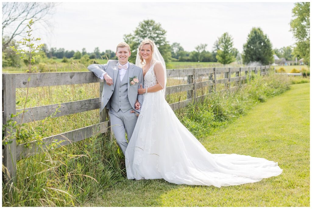 groom leaning against a wooden fence with bride holding onto his arm in Ohio