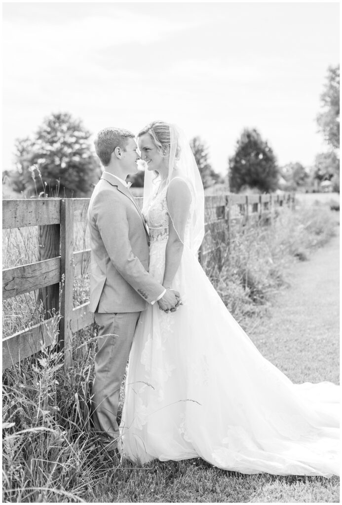 wedding couple holding hands and standing next to a wooden fence on the venue property