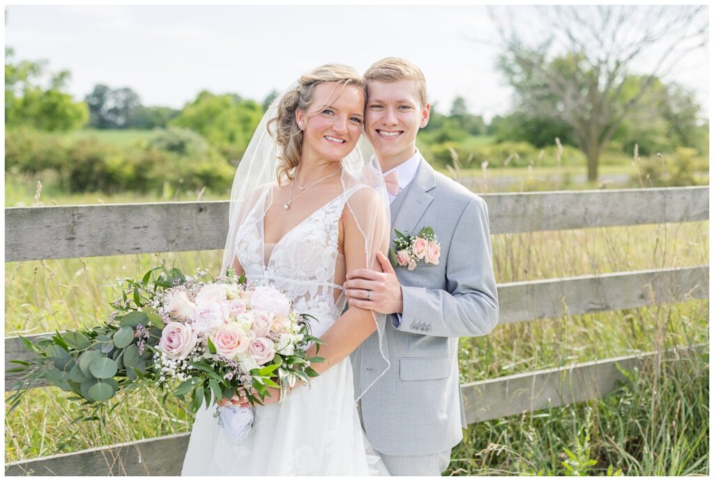 wedding couple posing next to a wooden fence on the venue property in Ohio