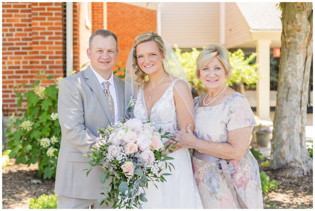 groom posing with her dad and stepmom before her wedding in Dublin, Ohio