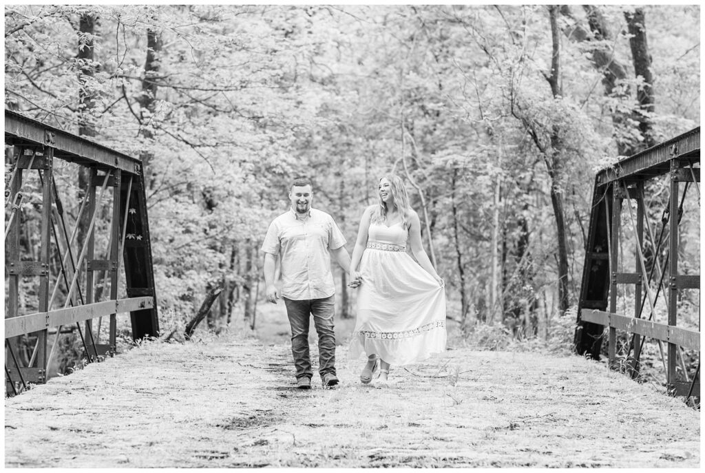 engaged couple walking across an old grass covered bridge in Ohio