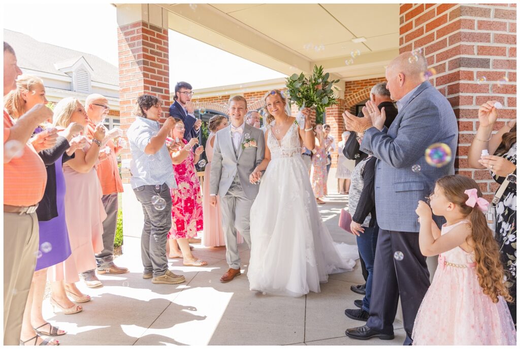 wedding guests cheering and blowing bubbles for the bride and groom as they leave the church