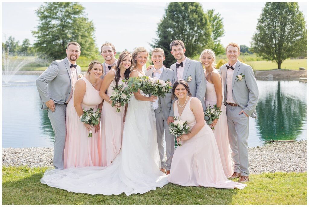 full wedding party posing together in front of the pond at Prairie Stone Farm venue