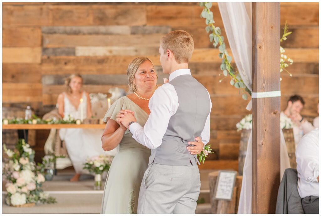 groom dancing with his mom at summer wedding reception while the bride looks on