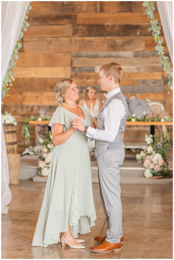 groom dancing with his mom inside the barn reception at Prairie Stone Farm as bride looks on