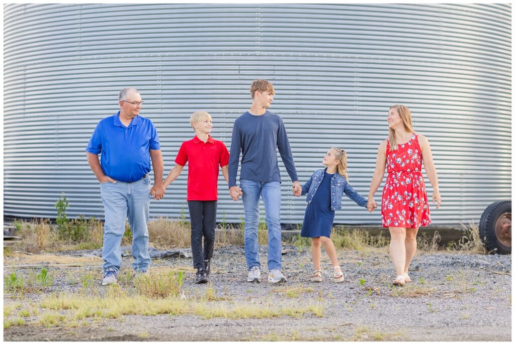 family wearing blues and reds walking hand in hand in front of a metal silo