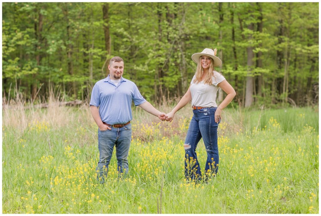 engagement couple holding hands in a yellow flower field in Willard, Ohio