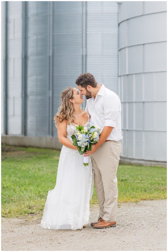 wedding couple touching noses and posing in front of a silo on the family farm