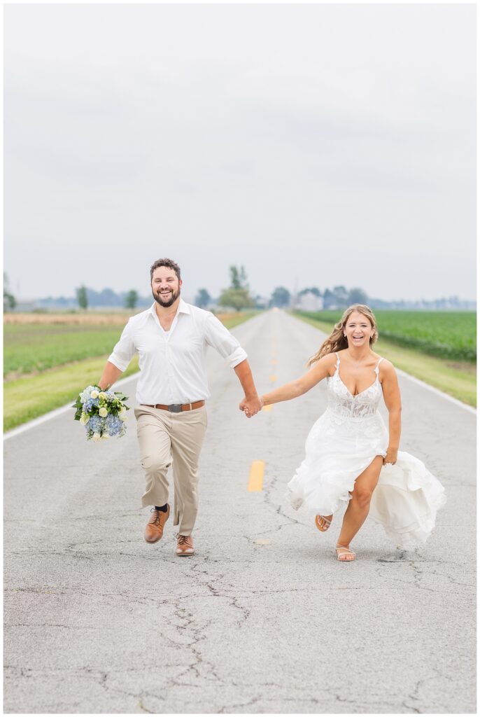 bride and groom running and holding hands in the middle of a road at country wedding