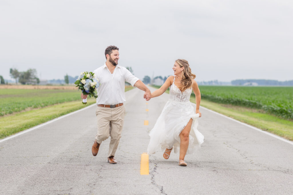 bride and groom running in the middle of the road next to a field 