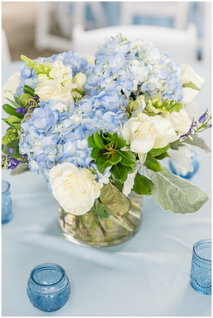 table centerpieces with white roses and blue hydrangeas in vases surrrounded by blue tea light holders