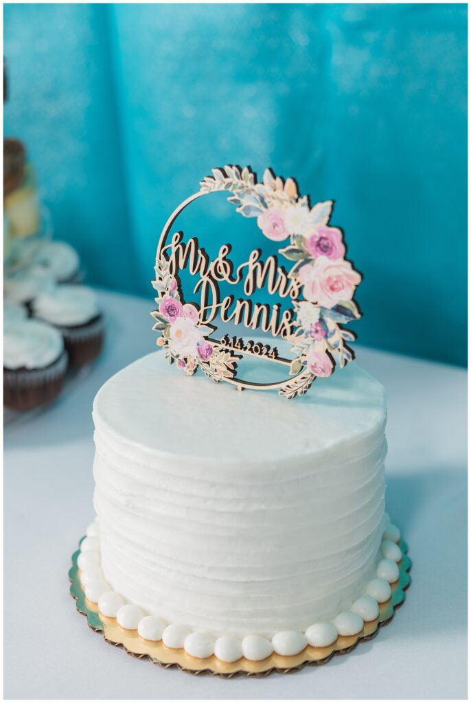 small white cake with topper of bride and groom's last name and wedding date