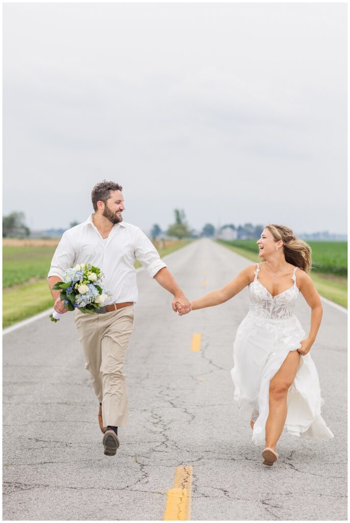 groom holding the bride's bouquet while running together in the middle of the road