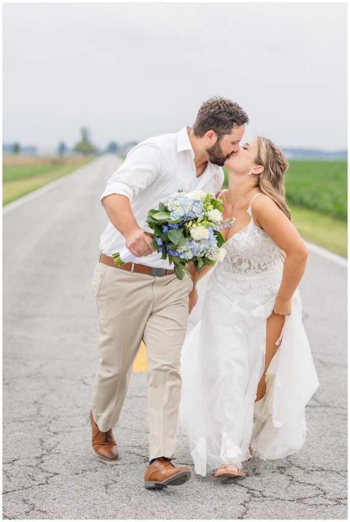 groom holding the bride's bouquet while kissing the bride at country wedding