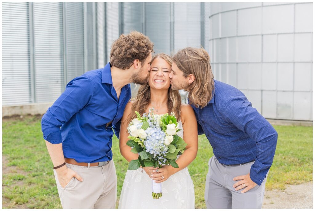 bride getting kissed on the cheek by her brothers at country wedding