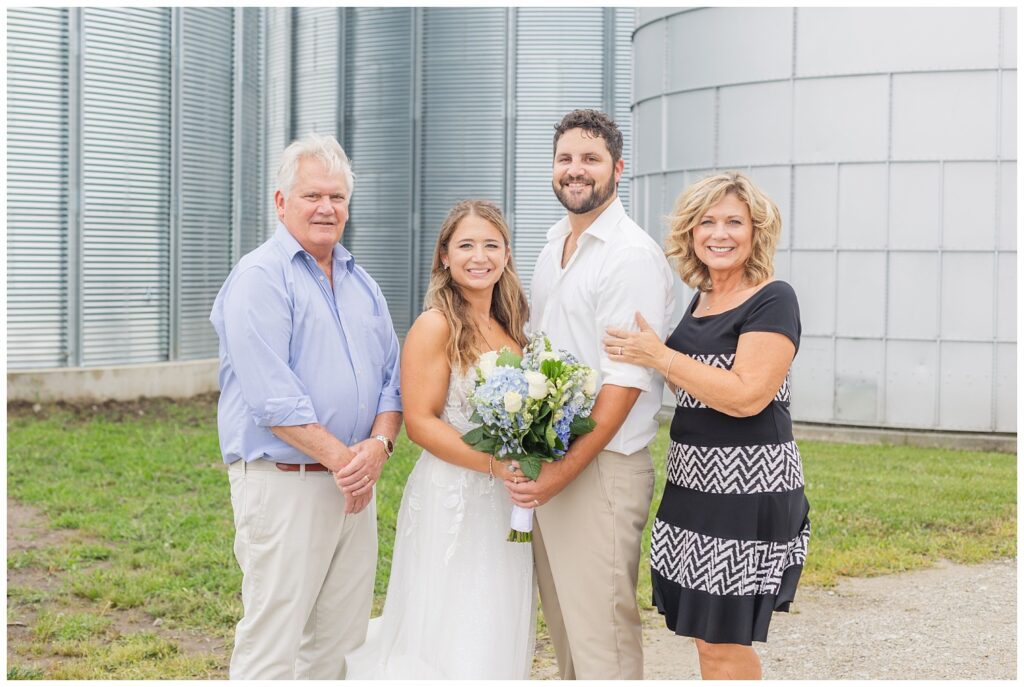 bride and groom posing with bride's parents in front of a silo at Ohio country wedding