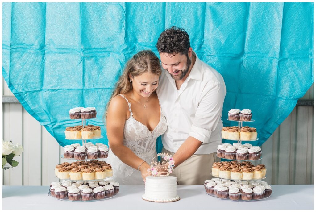 groom and bride cutting their cake in front of a blue decorations in family barn