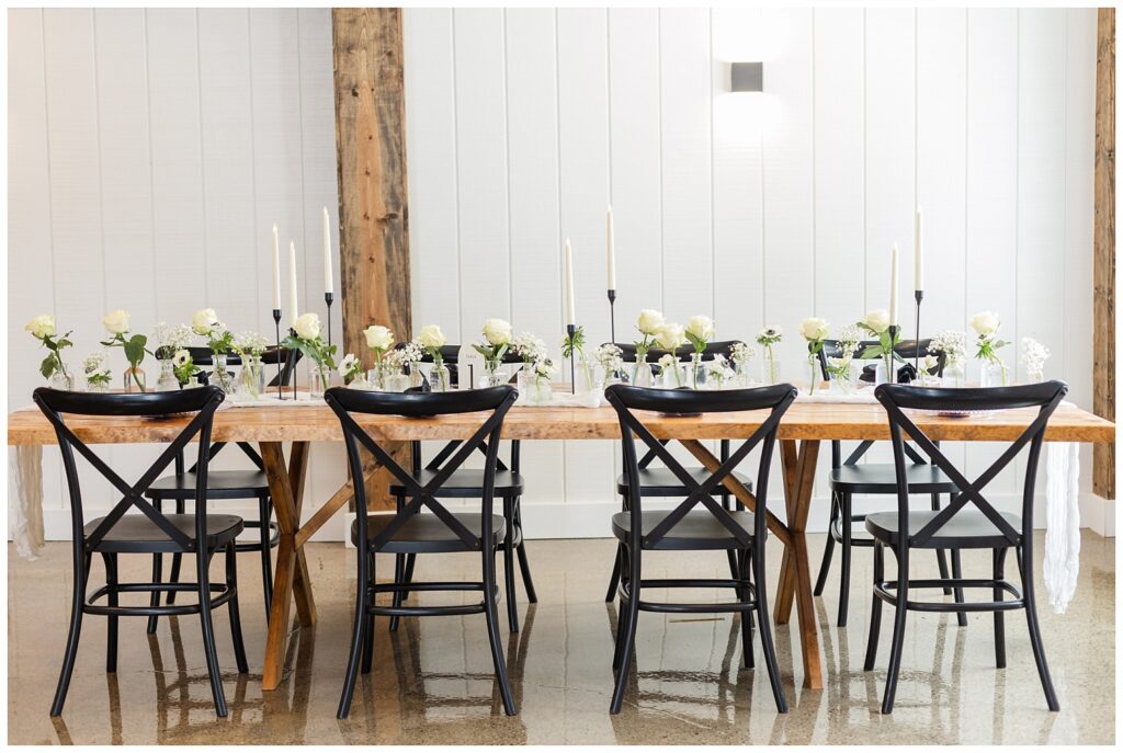 wooden table decorated with white table runner and black candlesticks in a barn