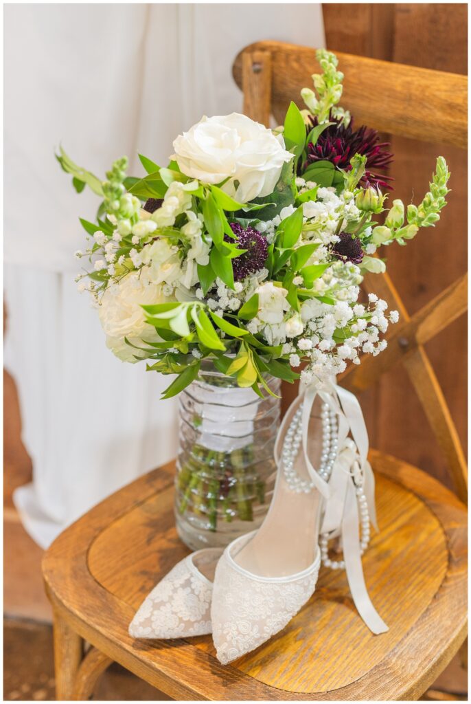 lace and pearl wedding shoes sitting on top of a wooden chair next to a vase of flowers 