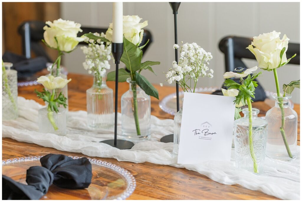 glass vases filled with white roses sitting on a gauze white table runner