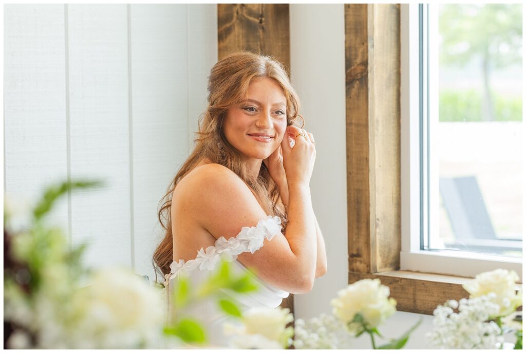 bride adjusting her earring next to a window in the barn venue in Tiffin, Ohio