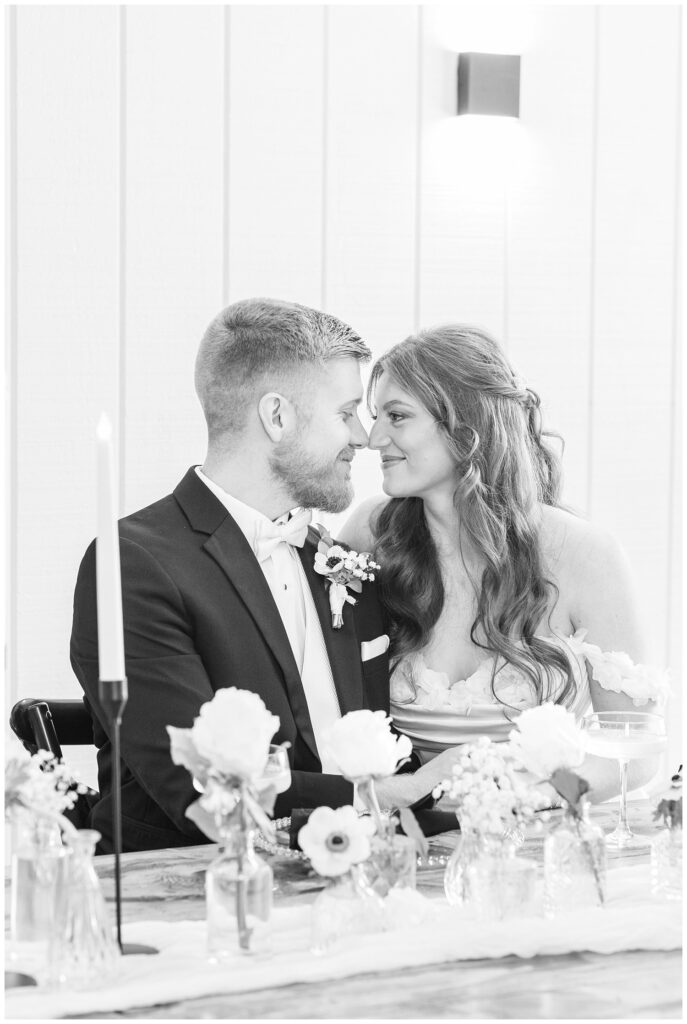 bride and groom touching noses while sitting at the reception table inside the venue