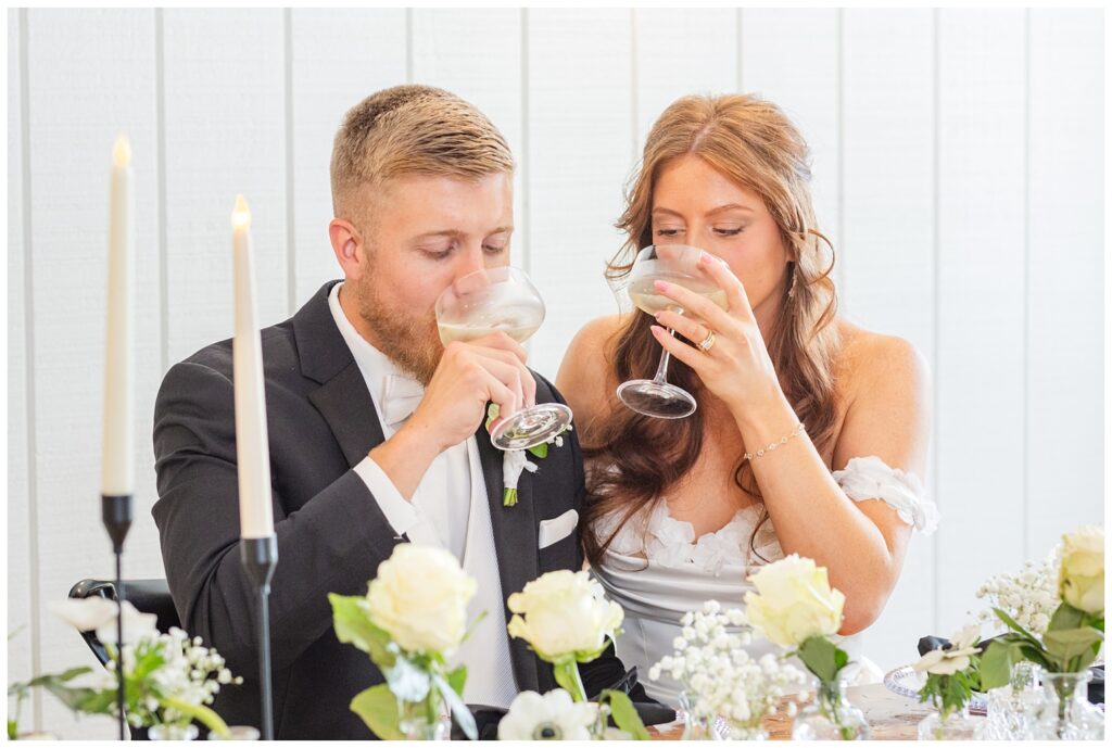 wedding couple drinking from their champagne glasses at the reception table at venue