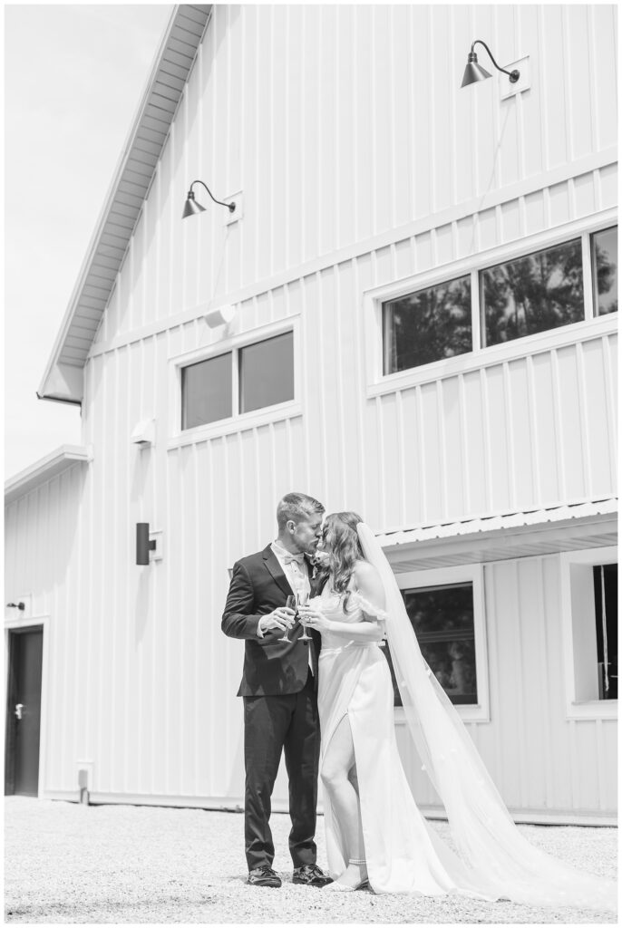 bride and groom kiss while toasting champagne flutes while standing on the patio