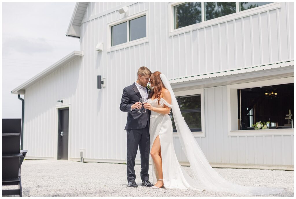 bride and groom toasting champagne flutes while standing on the patio at white barn venue