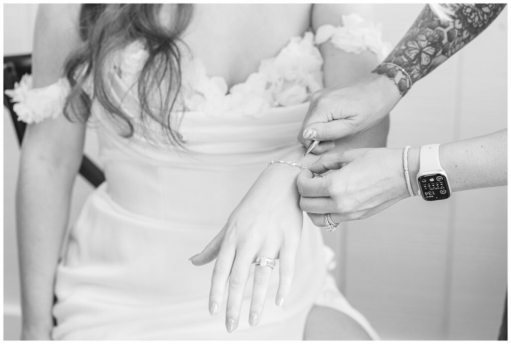 bride getting permanent jewelry put on next a window at wedding venue