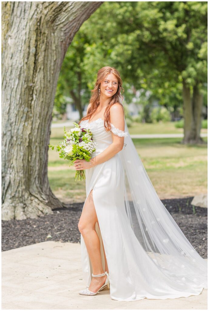 bride holding her bouquet on the patio in front of a large tree 