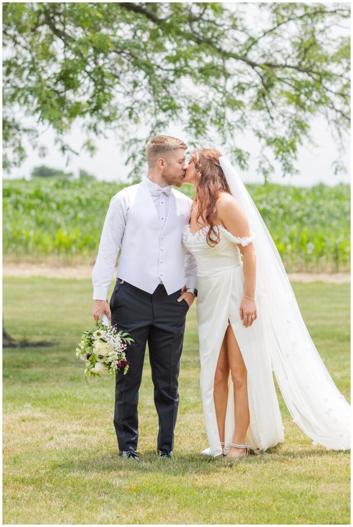 wedding couple share a kiss while groom holds the bride's bouquet