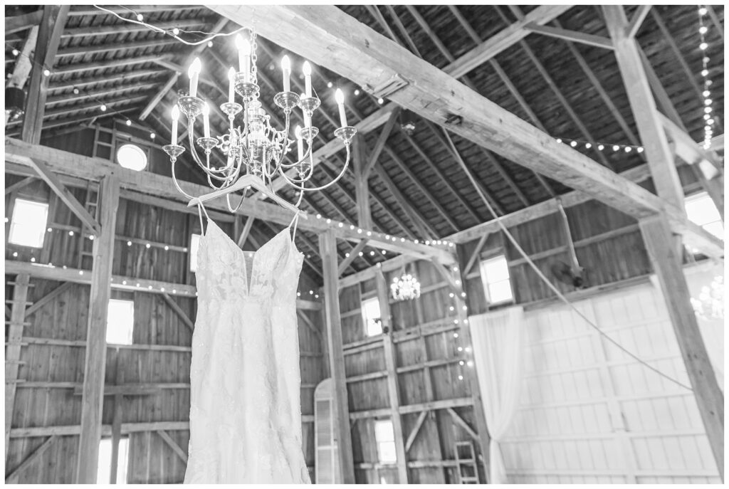 white lace wedding dress hanging from a chandelier in a barn