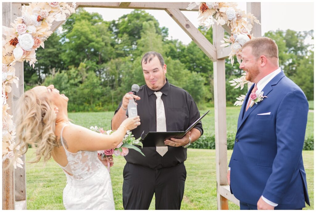 bride giving the officiant a beer during the ceremony at Arlington Acres