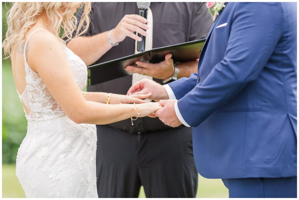 groom sliding the bride's ring onto her finger at Arlington Acres