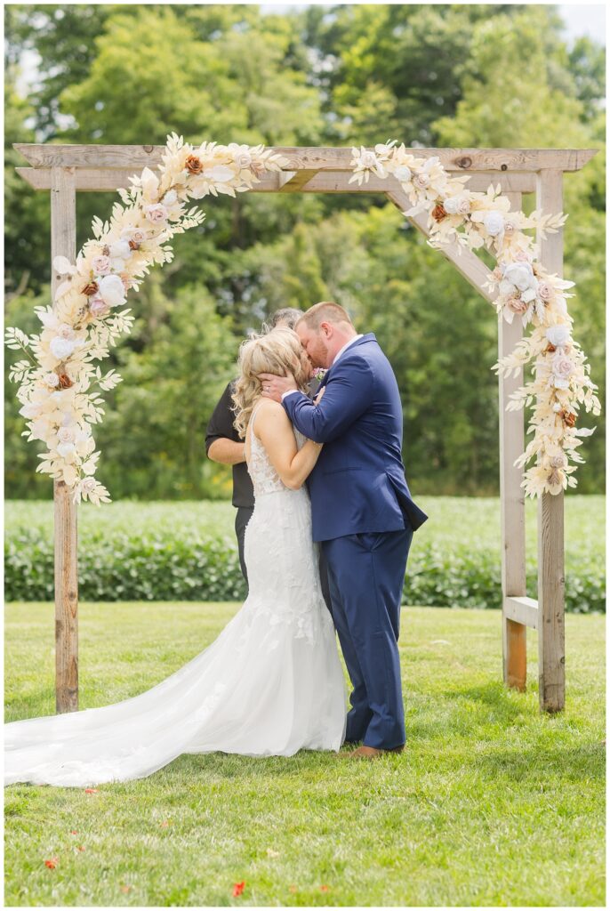 bride and groom kissing at the end of the ceremony surrounded by a wooden arch