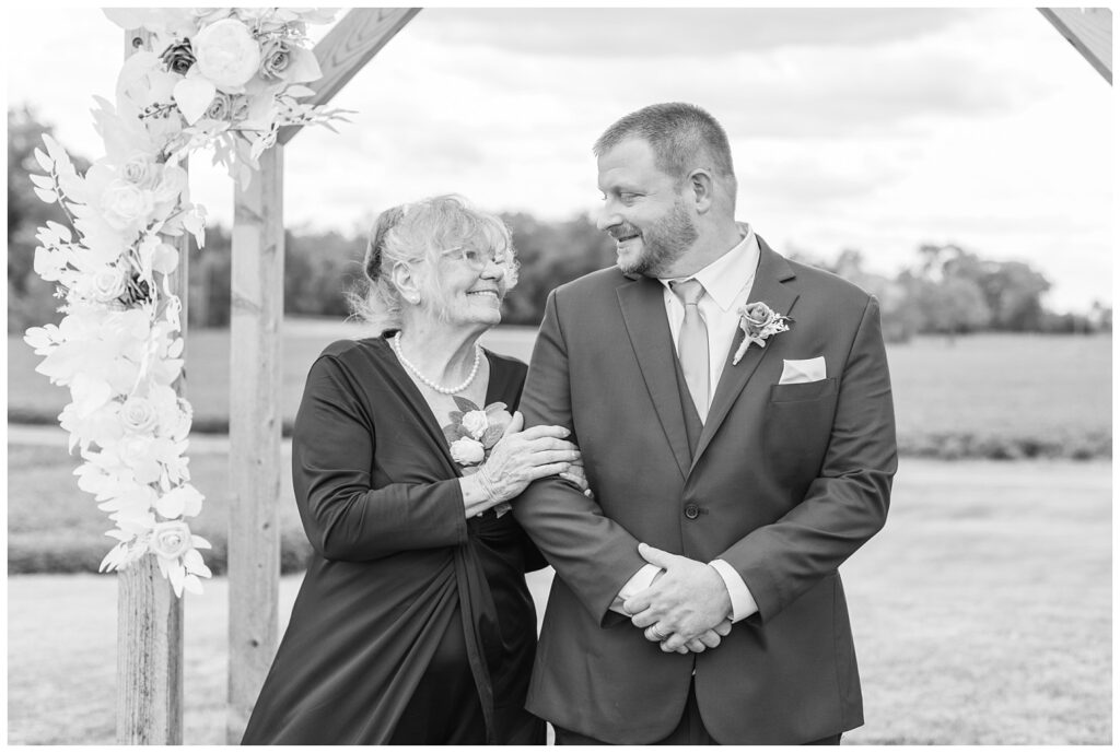 groom posing with his mom under the wooden arch at Arlington Acres