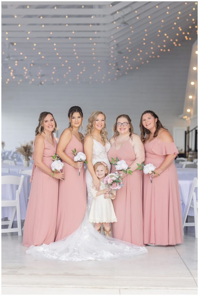 bridal party posing with the flower girl who is holding the bride's bouquet