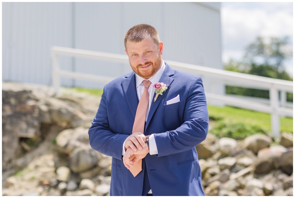 groom checking his watch next to the rock wall at Arlington Acres