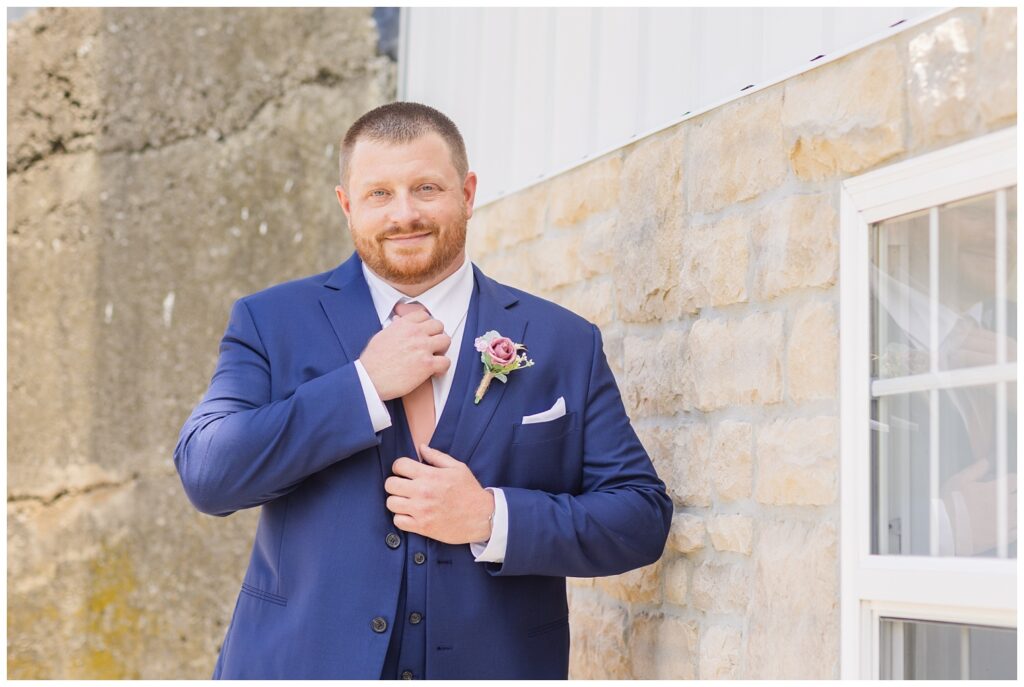 groom adjusting his tie next to a window outside at Arlington Acres