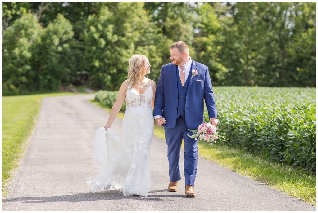 bride and groom walking on the road next to a field 