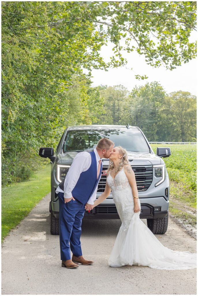 bride and groom kissing in front of the groom's gray truck