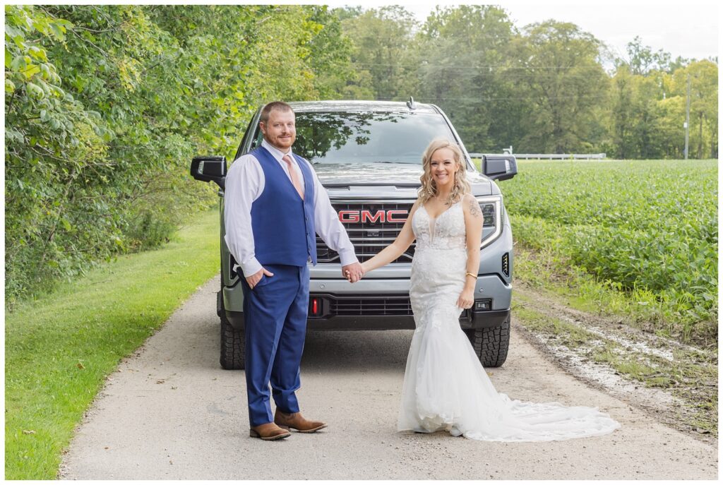 wedding couple posing together in front of the groom's truck 