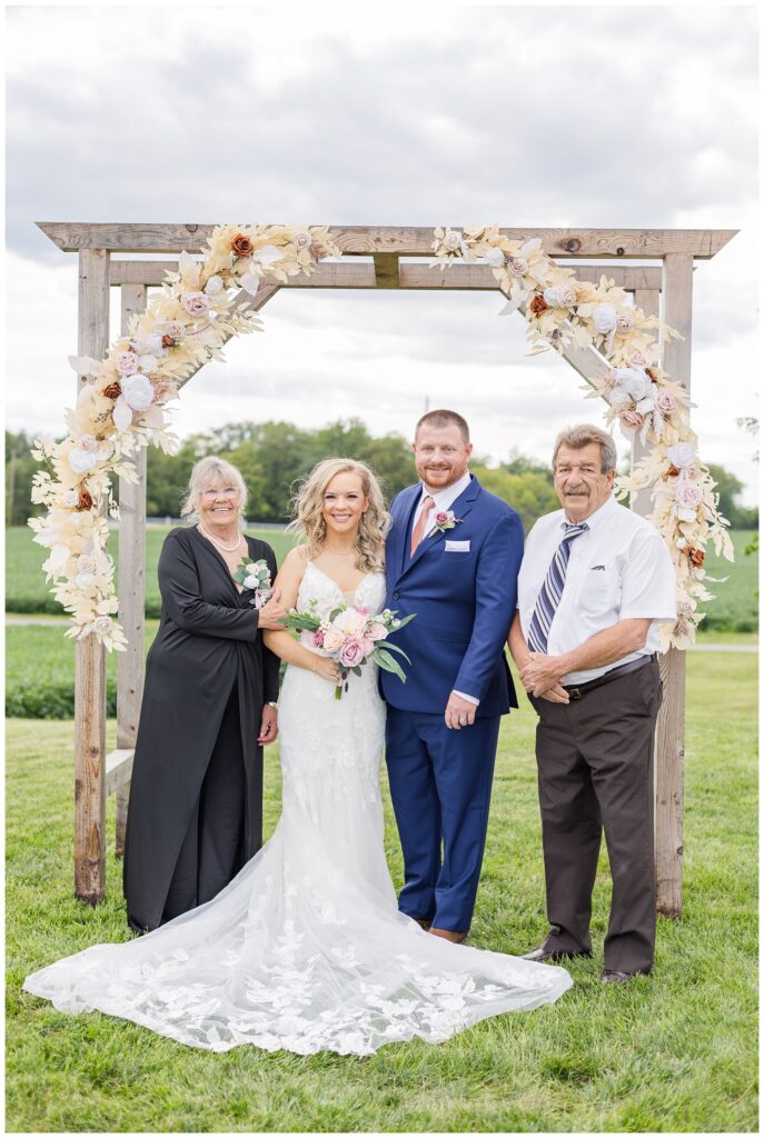 bride and groom posing with the groom's parents for family formals