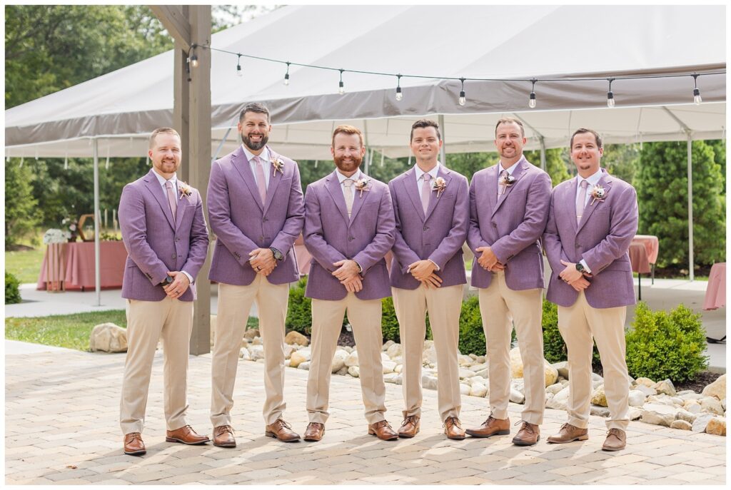 groomsmen posing together wearing purple jackets and khakis outside on the patio