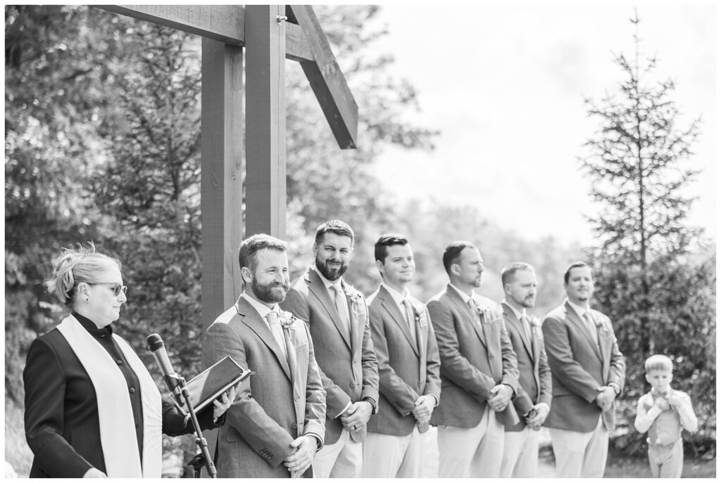 groom smiling at the bride walking down the aisle outside at wedding venue