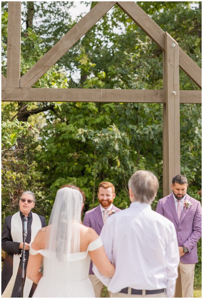 groom smiling at the bride and her dad as they approach the altar